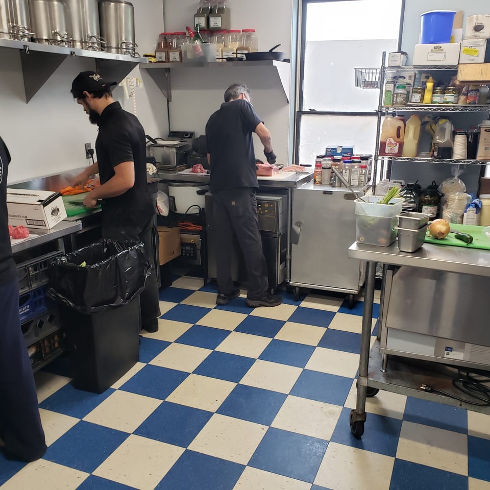 Chefs prepare food in a busy commercial kitchen with blue and white checkered floors.