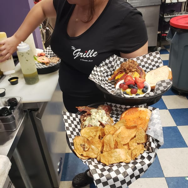 A server from The Grille at Franklin Court holds two baskets of food, including burgers, chips, and fruit.