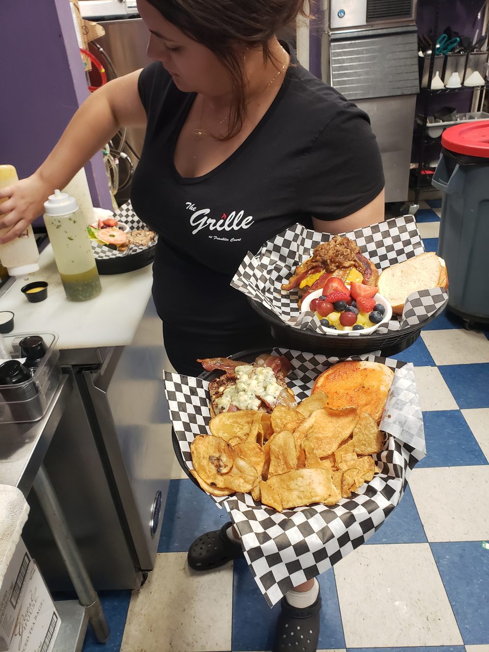 A server from The Grille at Franklin Court holds two baskets of food, including burgers, chips, and fruit.