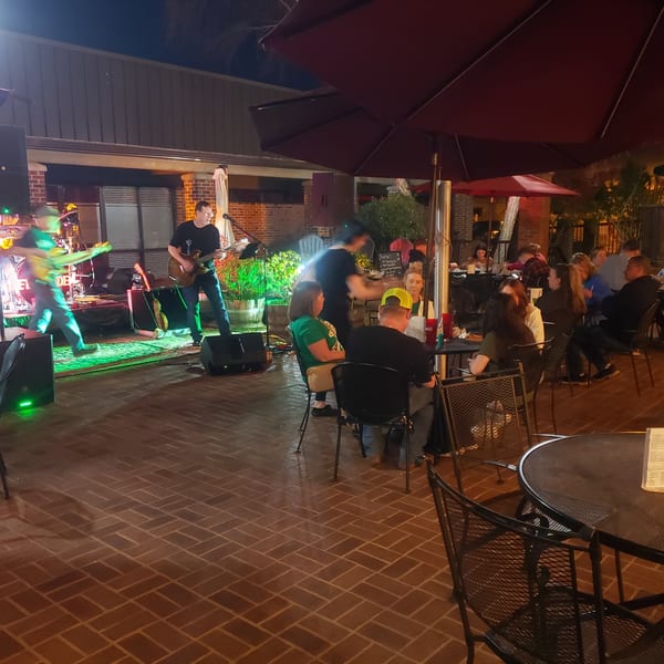 Outdoor patio at night with a live band performing for seated guests under umbrellas.