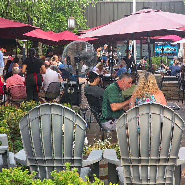Patrons enjoying live music and dining under red umbrellas on a restaurant's outdoor patio.